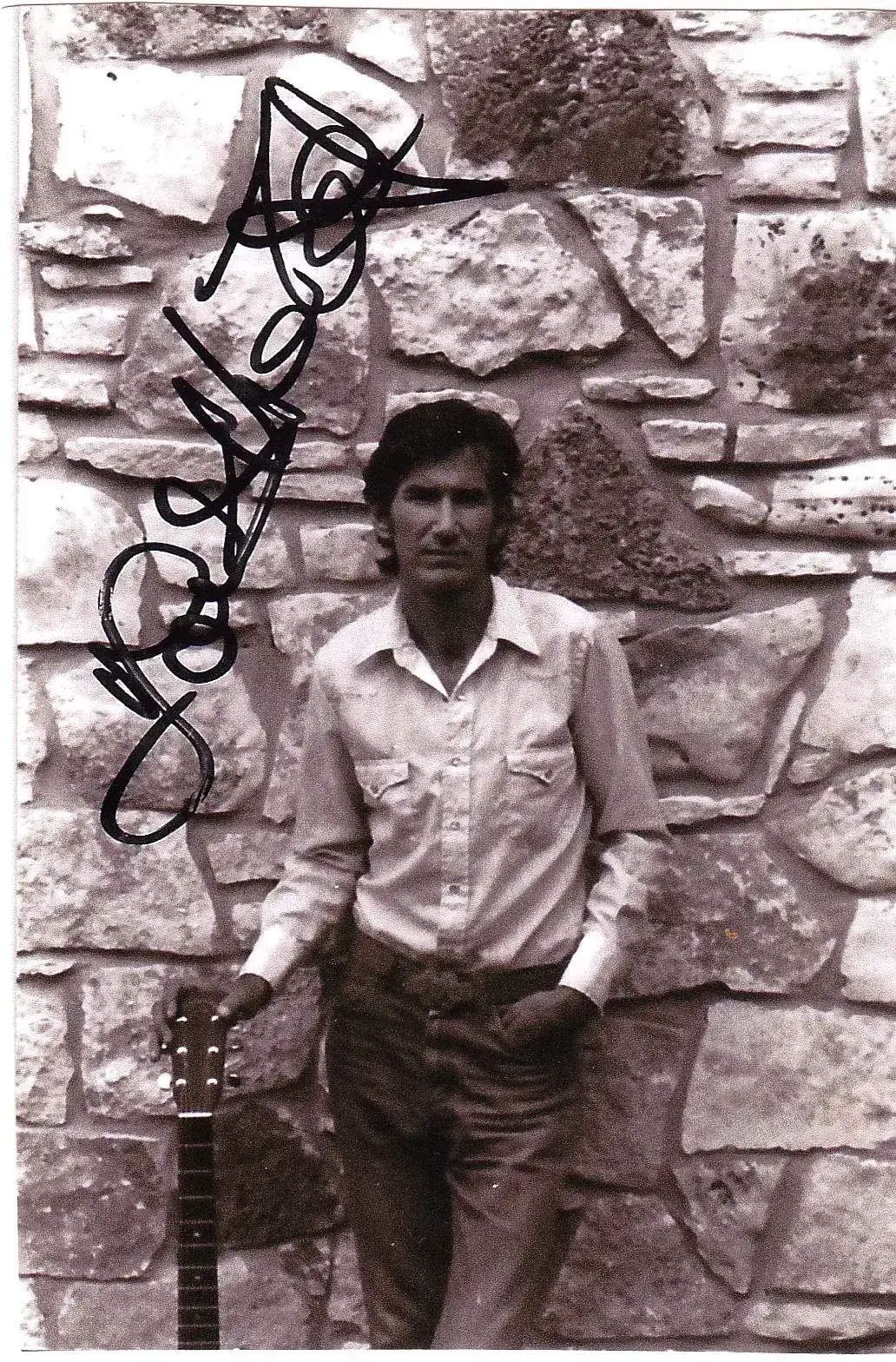 A man standing in front of a stone wall holding a guitar.